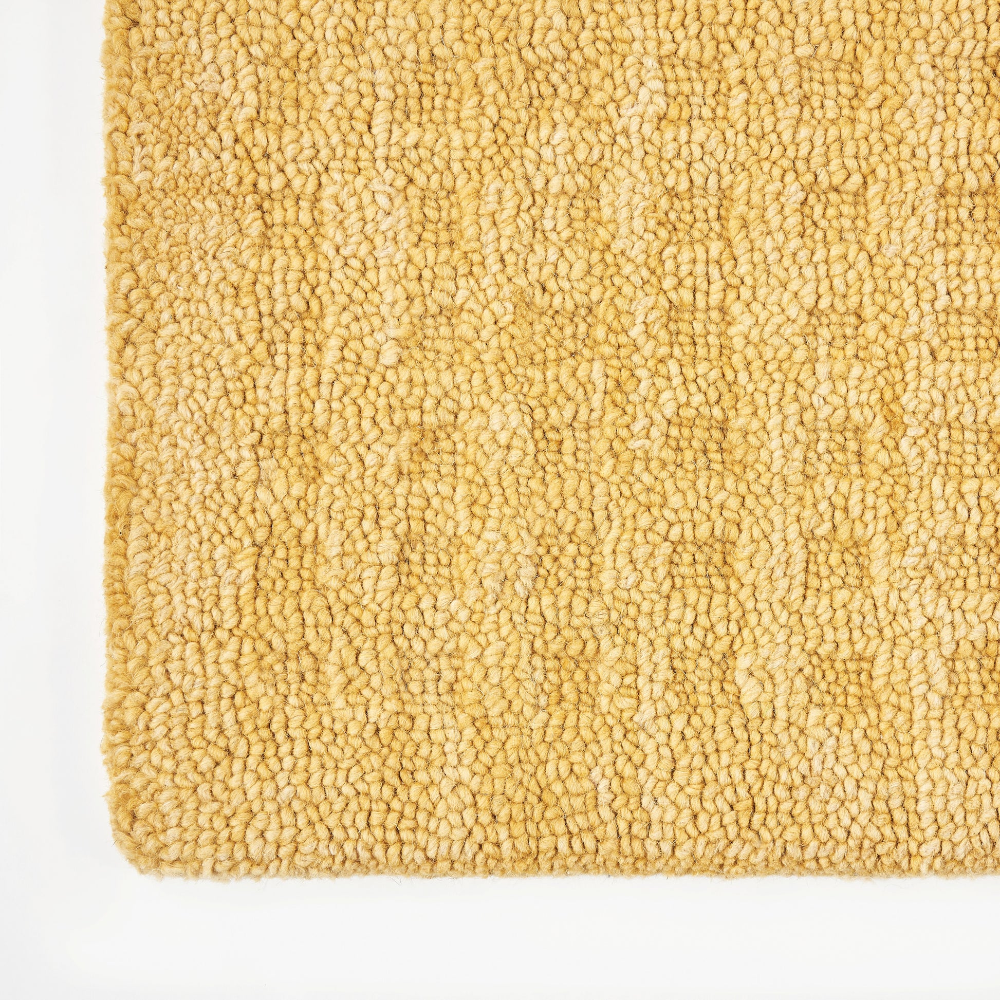 Golden beige boucle rug close-up with looped pile; soft textured floor mat for cozy interiors.