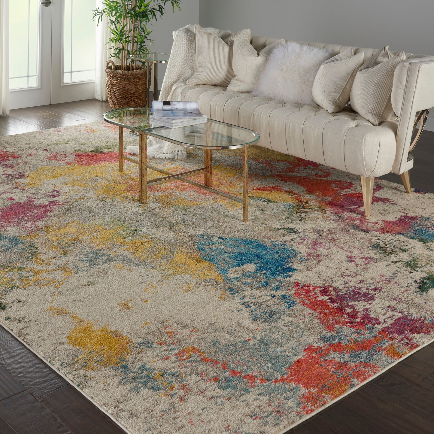 Beige tufted sofa with white fluffy cushion, glass oval coffee table, and a multicolor abstract rug in a bright living room.