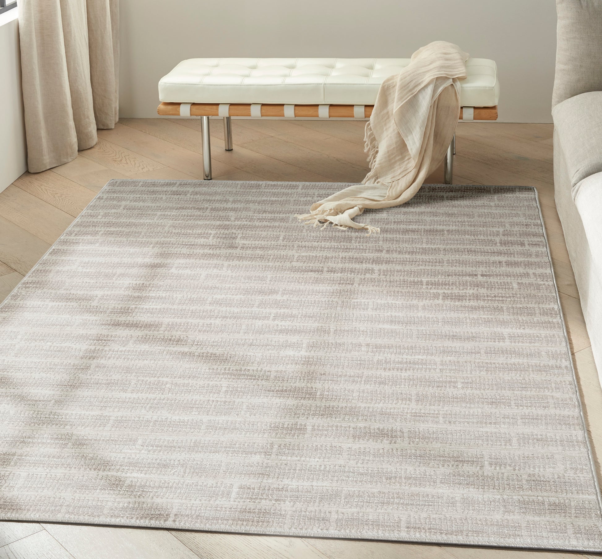Soft neutral beige flatweave rug with a subtle pattern on light wood floor, white tufted bench and beige throw.