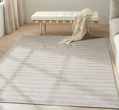 Soft neutral beige flatweave rug with a subtle pattern on light wood floor, white tufted bench and beige throw.