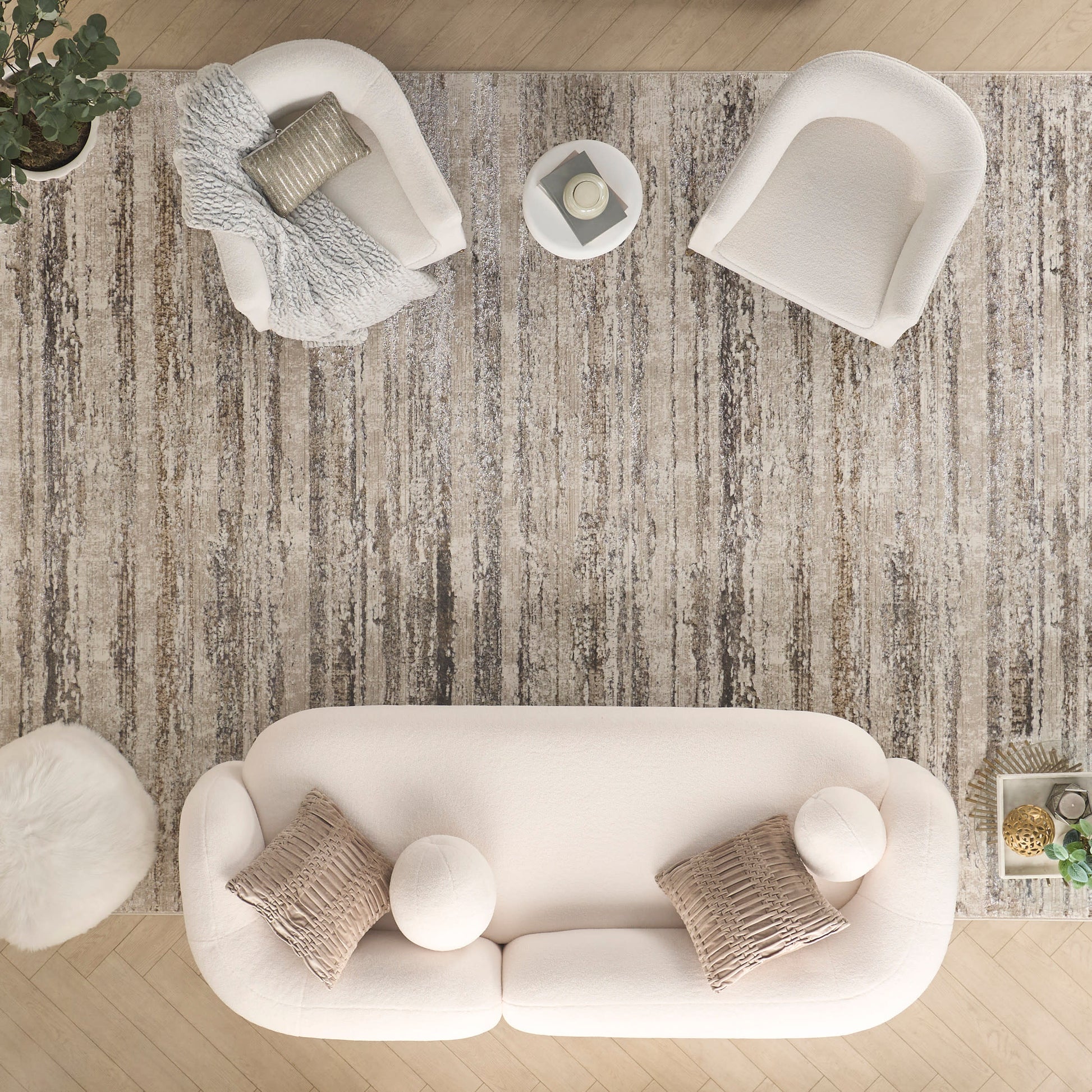 Overhead view of a cream fabric sofa with round pillows on a textured beige rug, paired with white armchairs and round ottomans.