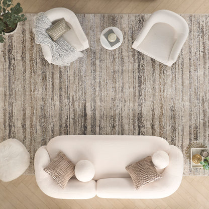 Overhead view of a cream fabric sofa with round pillows on a textured beige rug, paired with white armchairs and round ottomans.