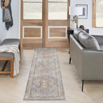 Long oriental-style rug runner in blue, ivory and peach tones laid through a living room between a gray sofa and bench.