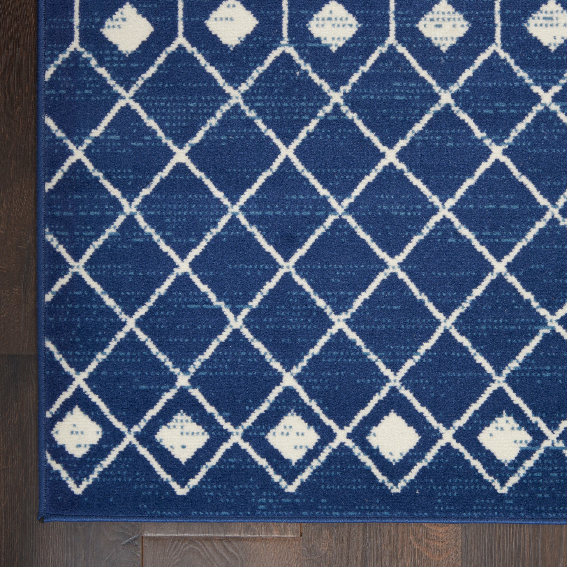 Blue rug with white diamond lattice pattern and small white diamonds on dark wood floor.
