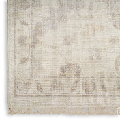 Cream woven rug with a subtle floral border pattern and fringe along the edge.