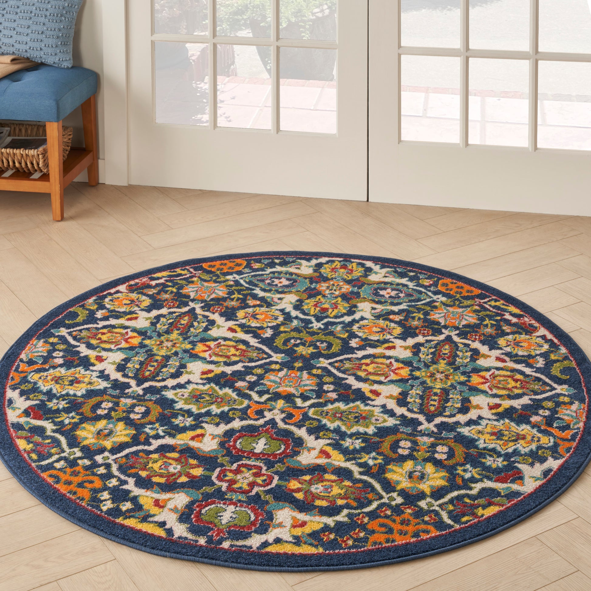 Round rug with navy border and vivid multicolor floral pattern in greens, yellows, oranges on light wood floor.