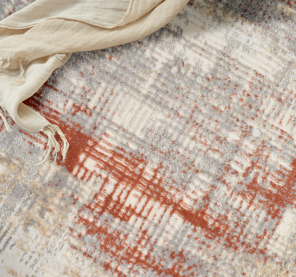 Abstract area rug in cream, gray & rust orange with fringed edge; beige scarf draped atop.