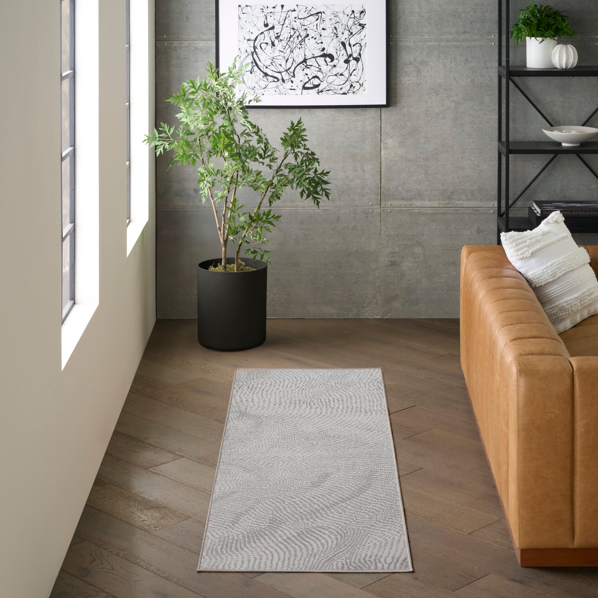 Gray rectangular runner rug with subtle pattern on herringbone wood floor beside a brown leather sofa and potted plant.