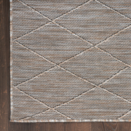 Beige woven rug featuring a geometric diamond pattern with fringe along the edge on dark wood floor.