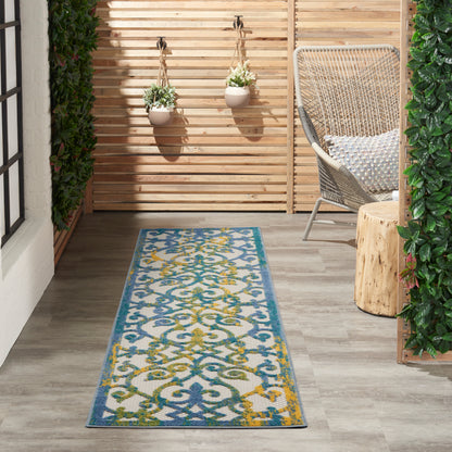 Outdoor balcony with blue patterned runner rug, wicker chair, wooden stump table, hanging planters, privacy slat wall.