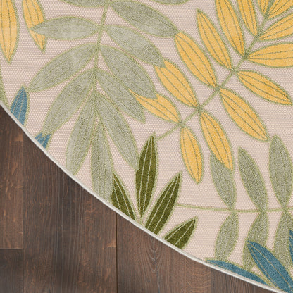 Beige rectangular rug with green, yellow and blue botanical leaf pattern, curved edge on dark wood floor.