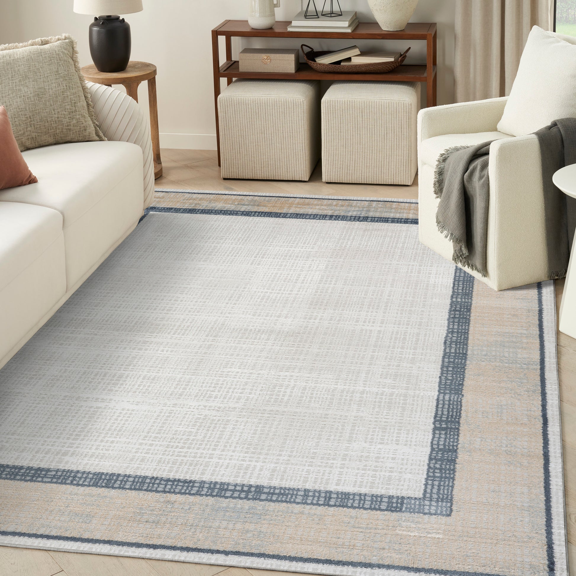 Rectangular ivory-gray woven area rug with blue inner border and beige outer border in a modern living room.