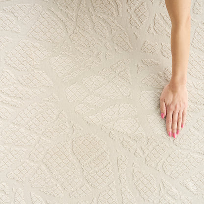 Beige textured area rug with raised diamond lattice pattern; hand with pink nails resting on it.