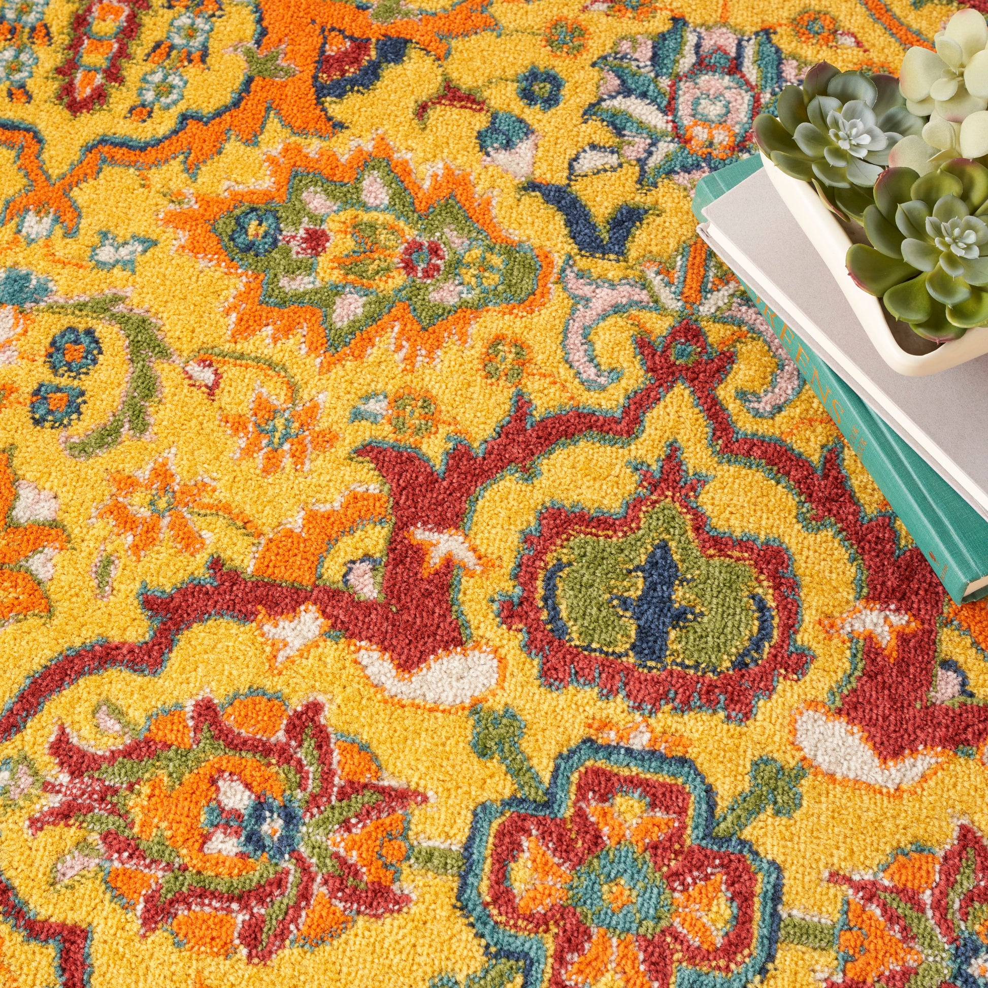 Vibrant yellow Oriental rug with red, blue and green floral motifs; stack of books beside a white-pot succulent.