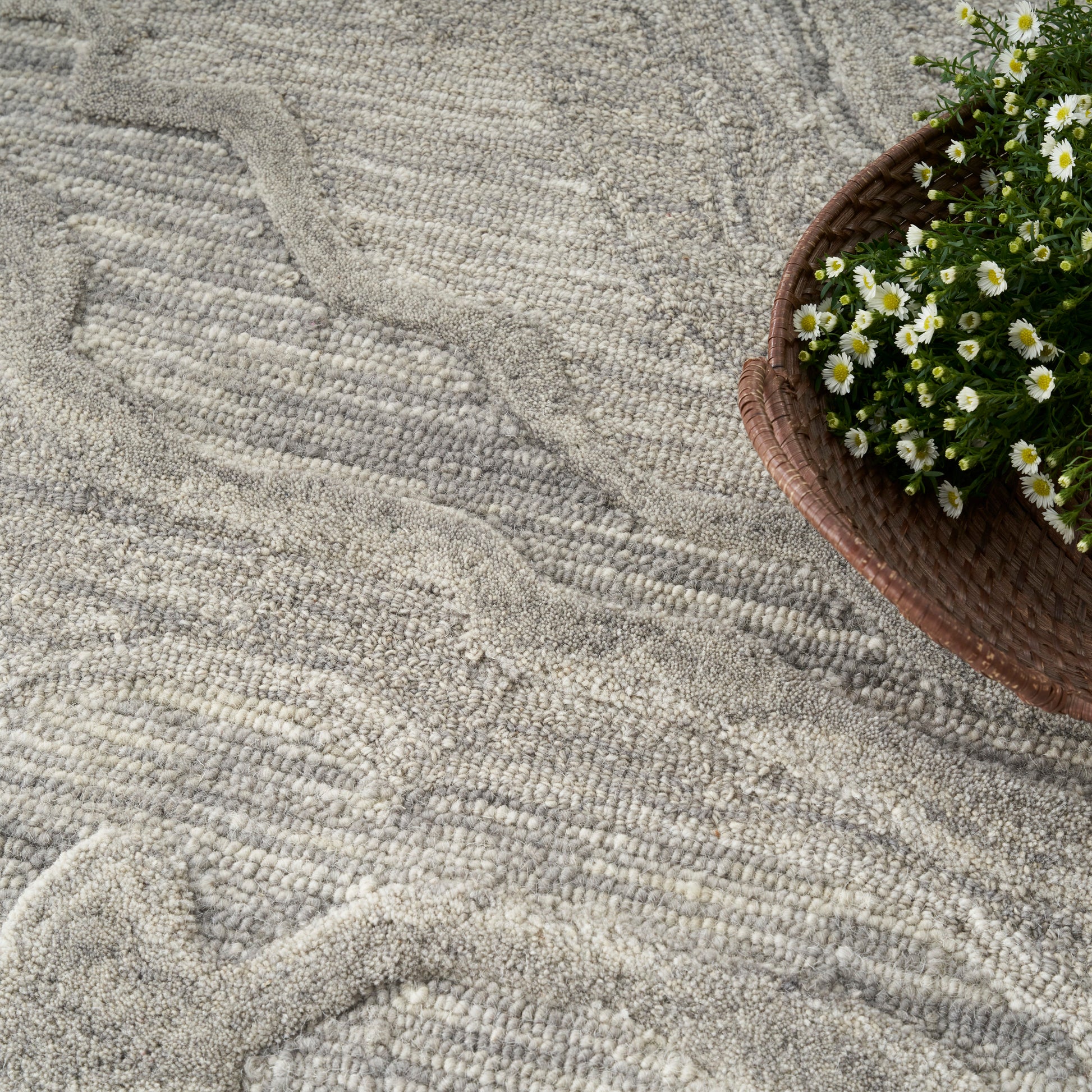 Grey textured rug with soft wavy pile; brown basket of white daisies sits along the edge.