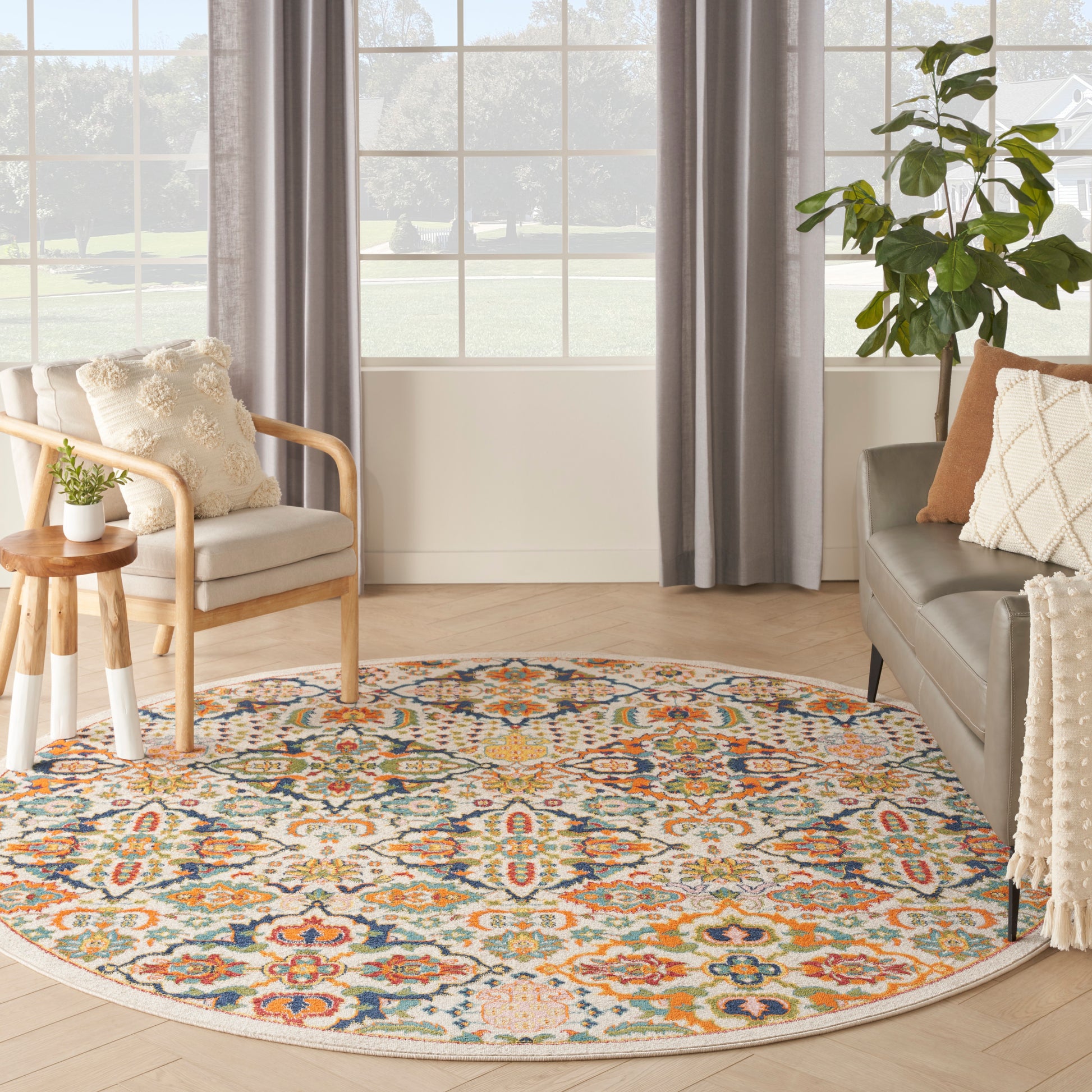 Round multicolor patterned rug on light wood floor, beige sofa and wooden chair in bright living room.