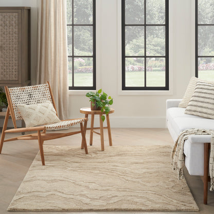 Neutral living room with woven lounge chair, round wood side table with plant, cream sofa, beige textured rug, grid windows