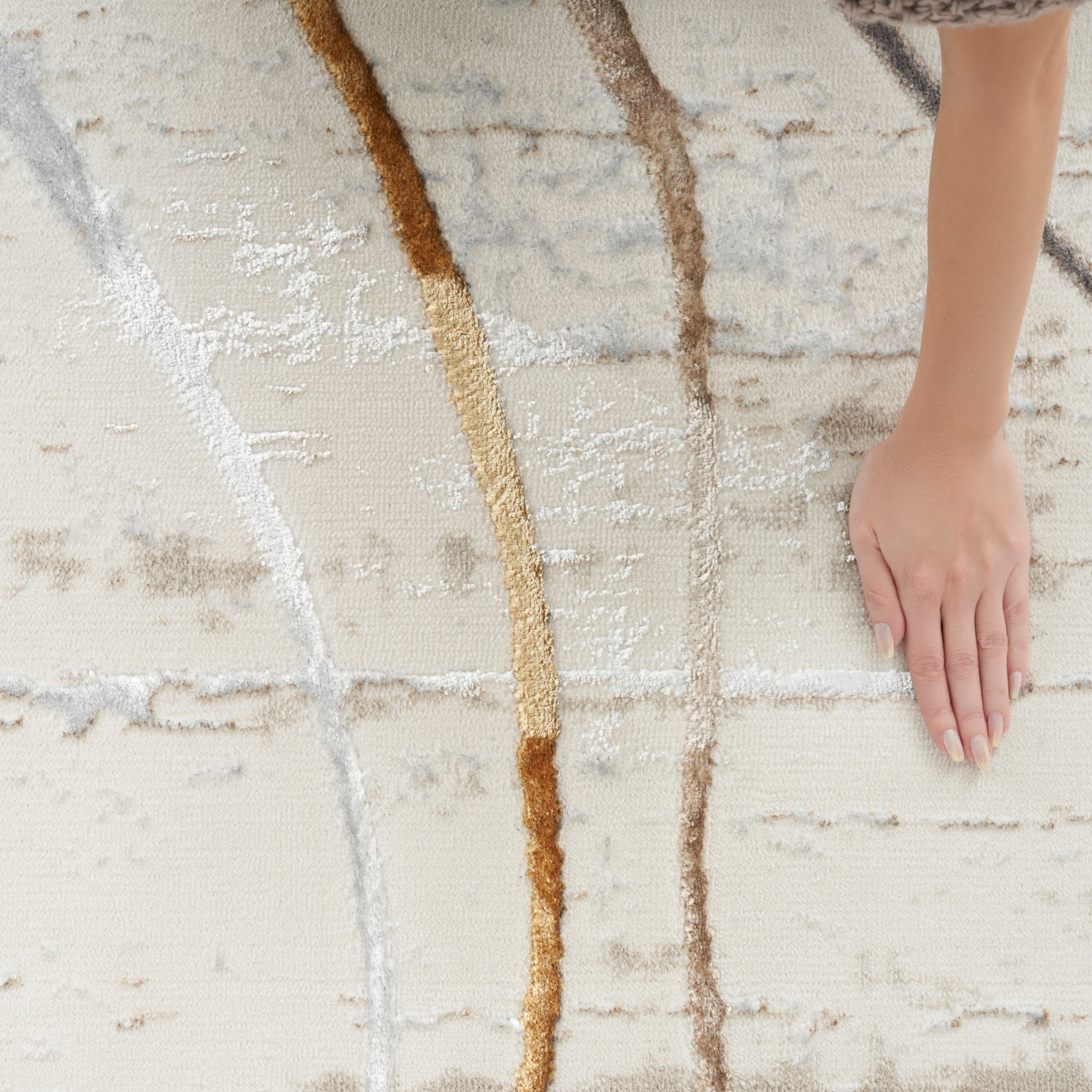 Beige textured runner rug with abstract brown and tan curved lines; a hand resting on the soft surface.