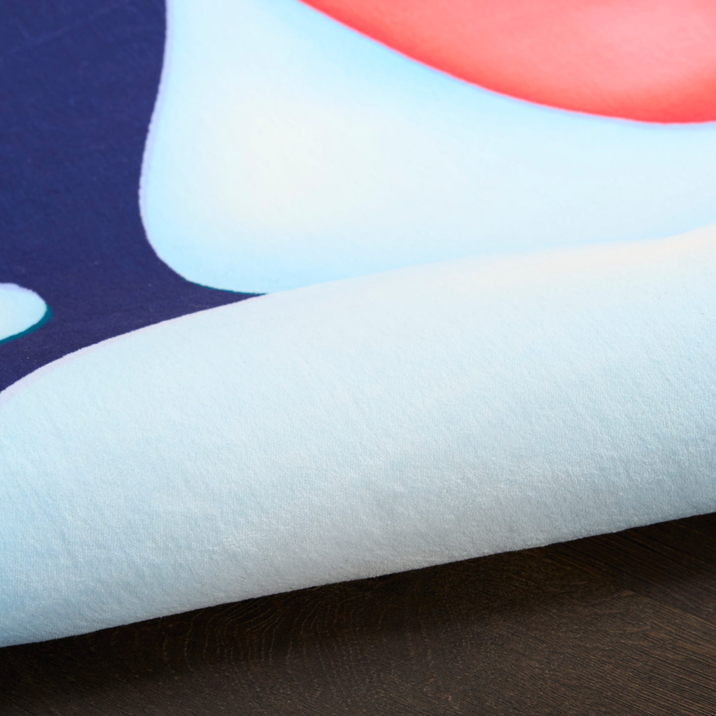 Close-up of an abstract textile print on a rug with a pale blue and white rolled edge, navy background and coral-orange curved accent.