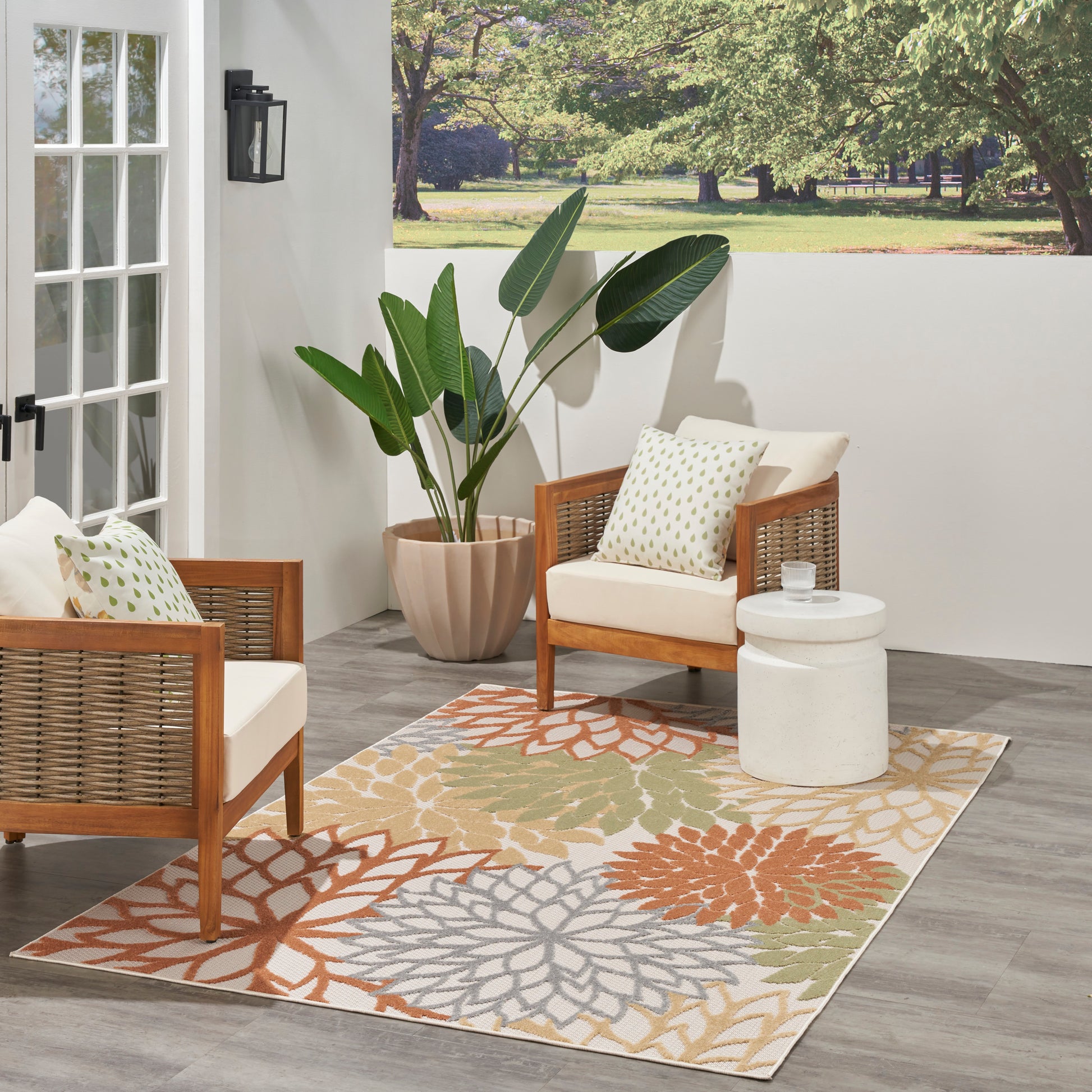 Outdoor patio with wicker armchairs, beige cushions, a multicolor floral rug (5' x 8'), a white round table, and a large potted plant.