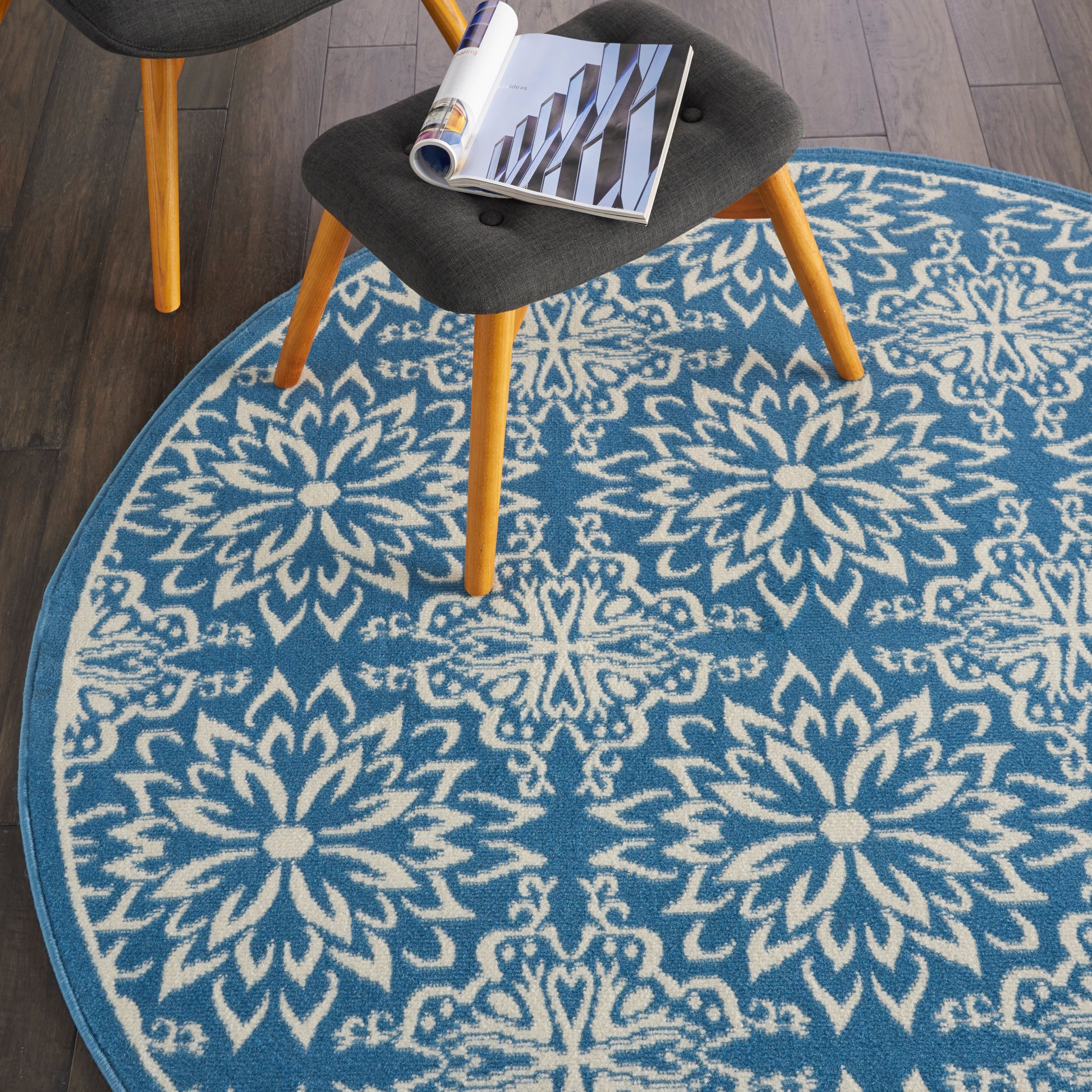 Round blue rug with white snowflake floral pattern; chair with light wood legs and a magazine on it.