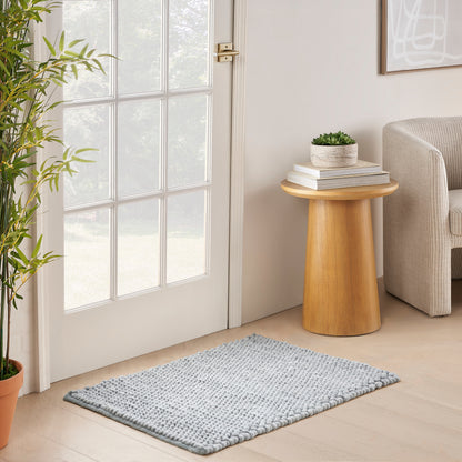 Cozy entry with glass-pane door, round wooden side table stacked with books and plant, beige armchair, light blue rug.