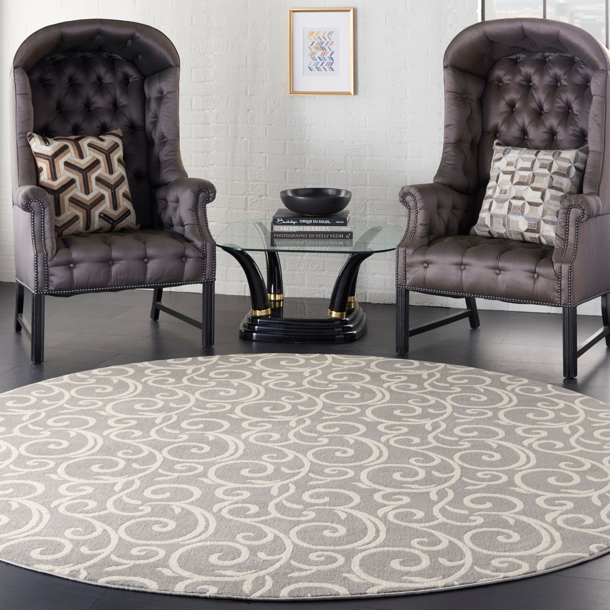 Pair of dark brown tufted wing chairs with nailhead trim, a round glass coffee table, and a gray swirled rug.