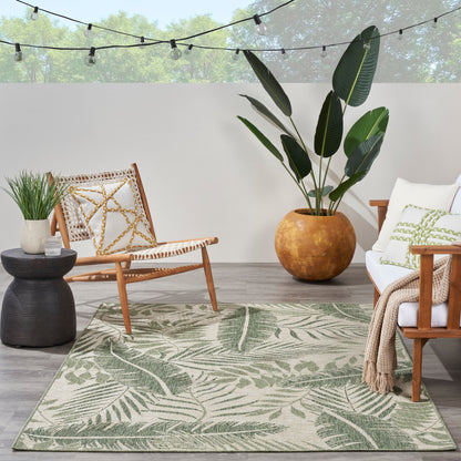 Outdoor tropical patio: palm-leaf rug, wooden chair, white cushions, large terracotta plant pot, string lights.