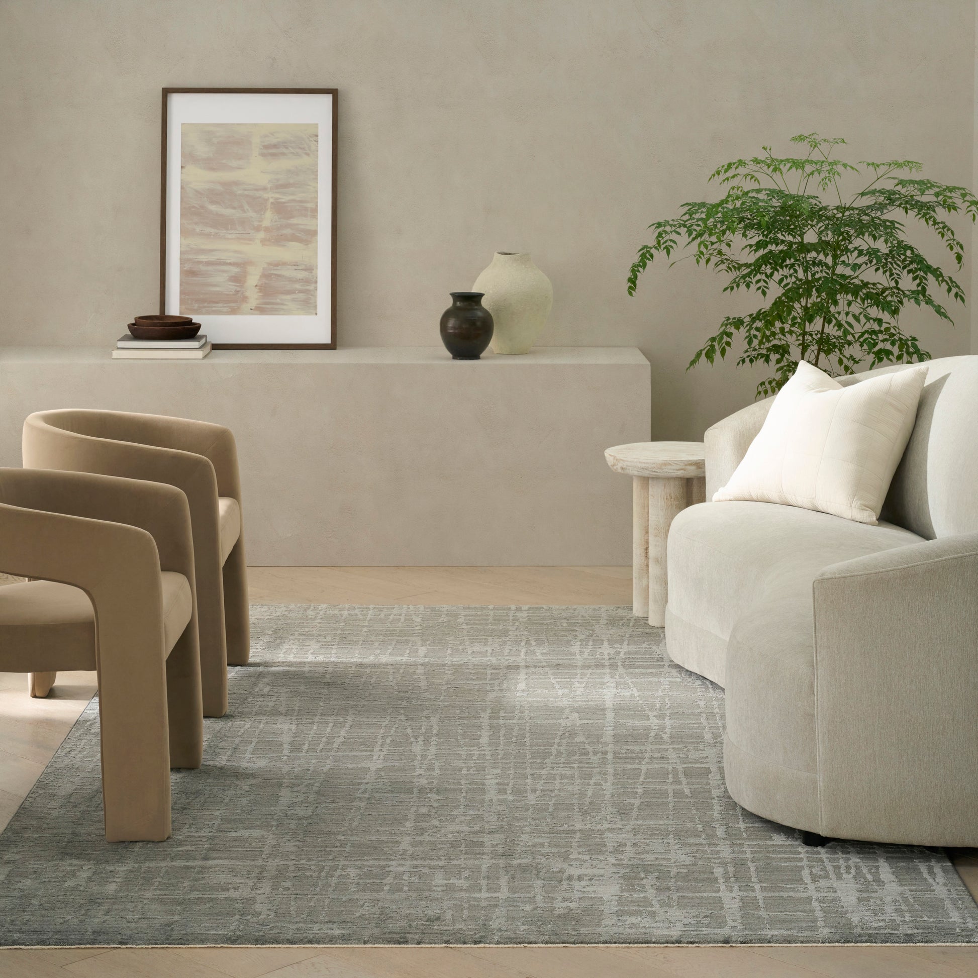 Neutral living room with beige curved chairs, light sofa, gray rug, wood side table, framed art, vases, and a potted plant.