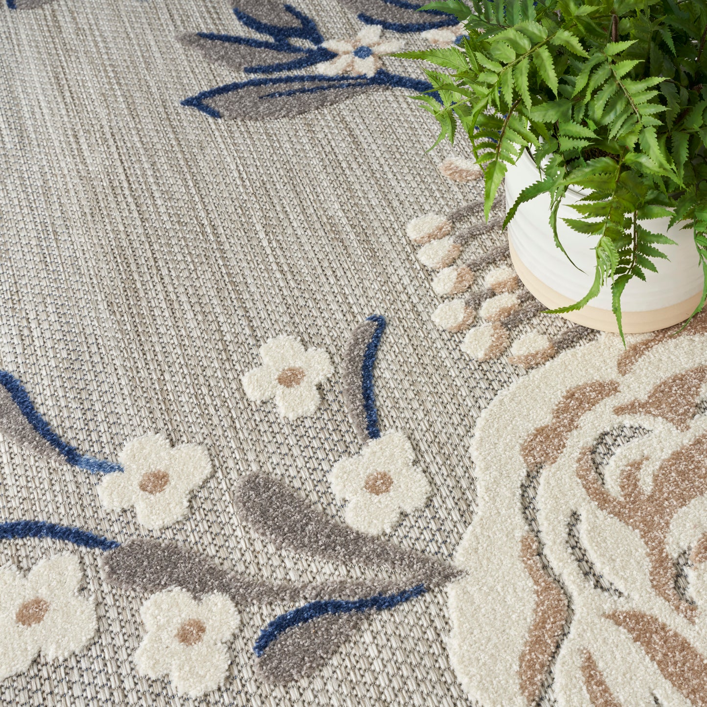 Woven neutral-toned area rug with cream floral motifs and blue stems on a gray-beige background; rustic-modern style.
