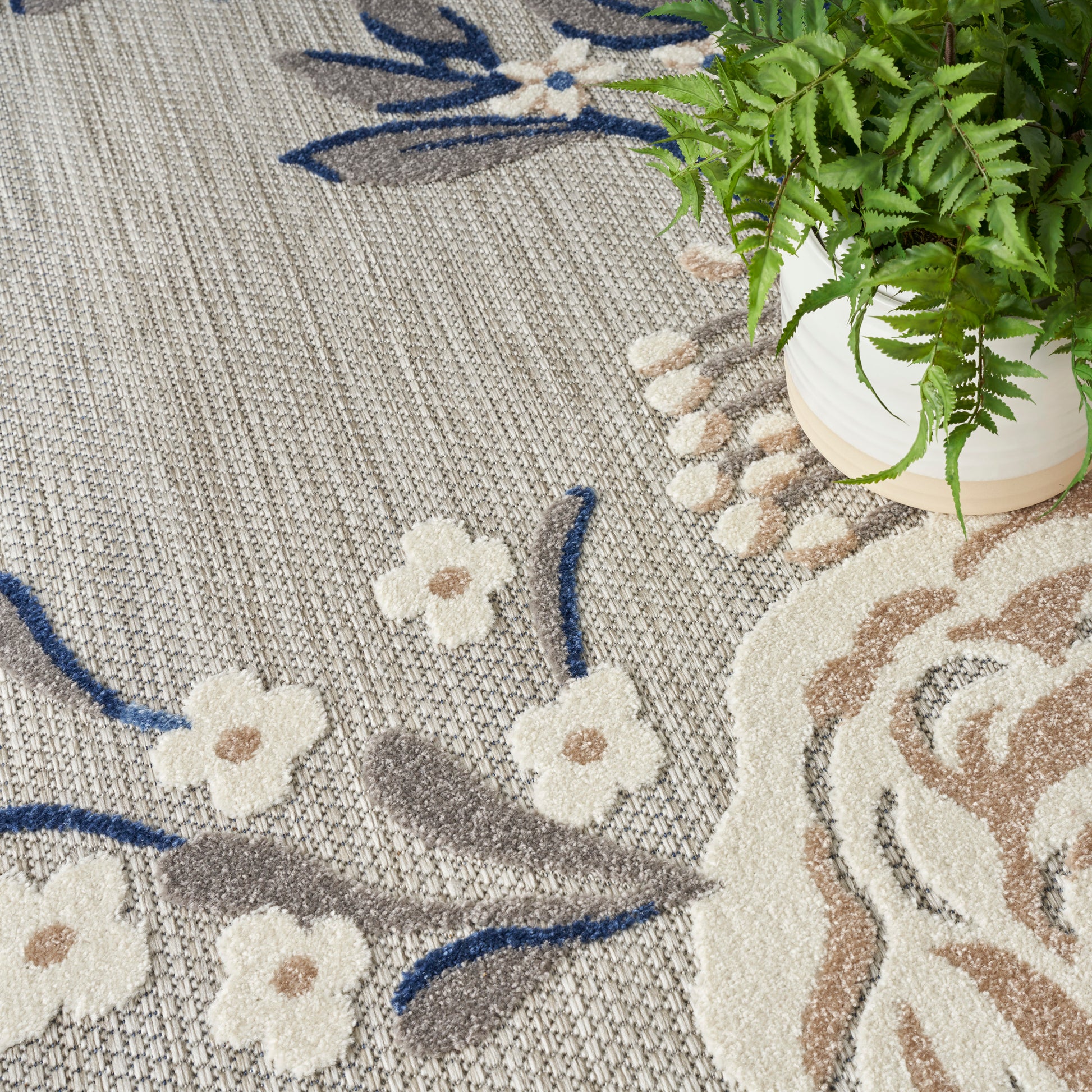 Woven neutral-toned area rug with cream floral motifs and blue stems on a gray-beige background; rustic-modern style.