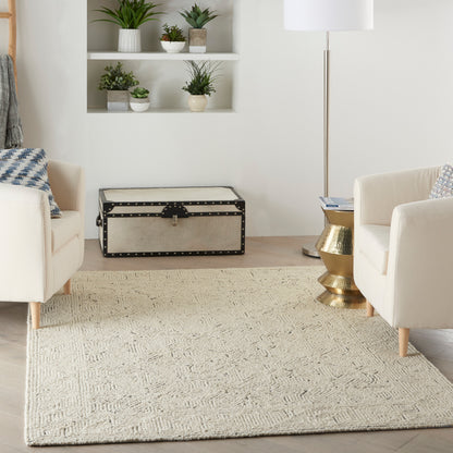 Cream upholstered chairs, beige woven rug, vintage studded trunk, brass side table, and potted plants in a living room.