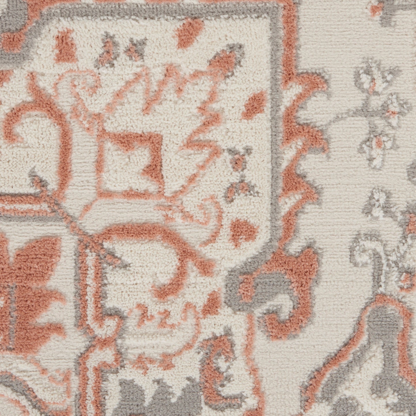 Close-up of an area rug with a cream base and coral-orange and gray ornate floral crest pattern.