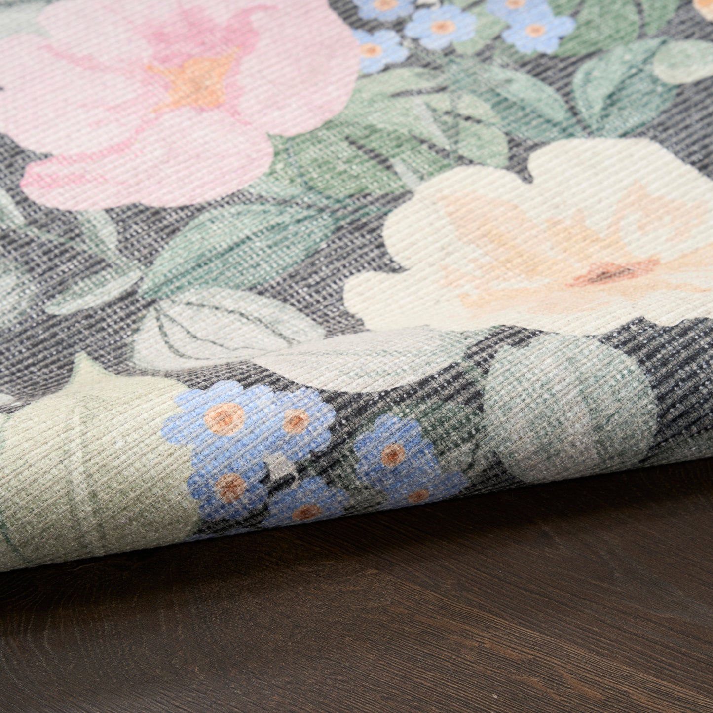 Floral print fabric with pink, peach, and blue flowers and green leaves; linen-like texture, folded edge on wood.