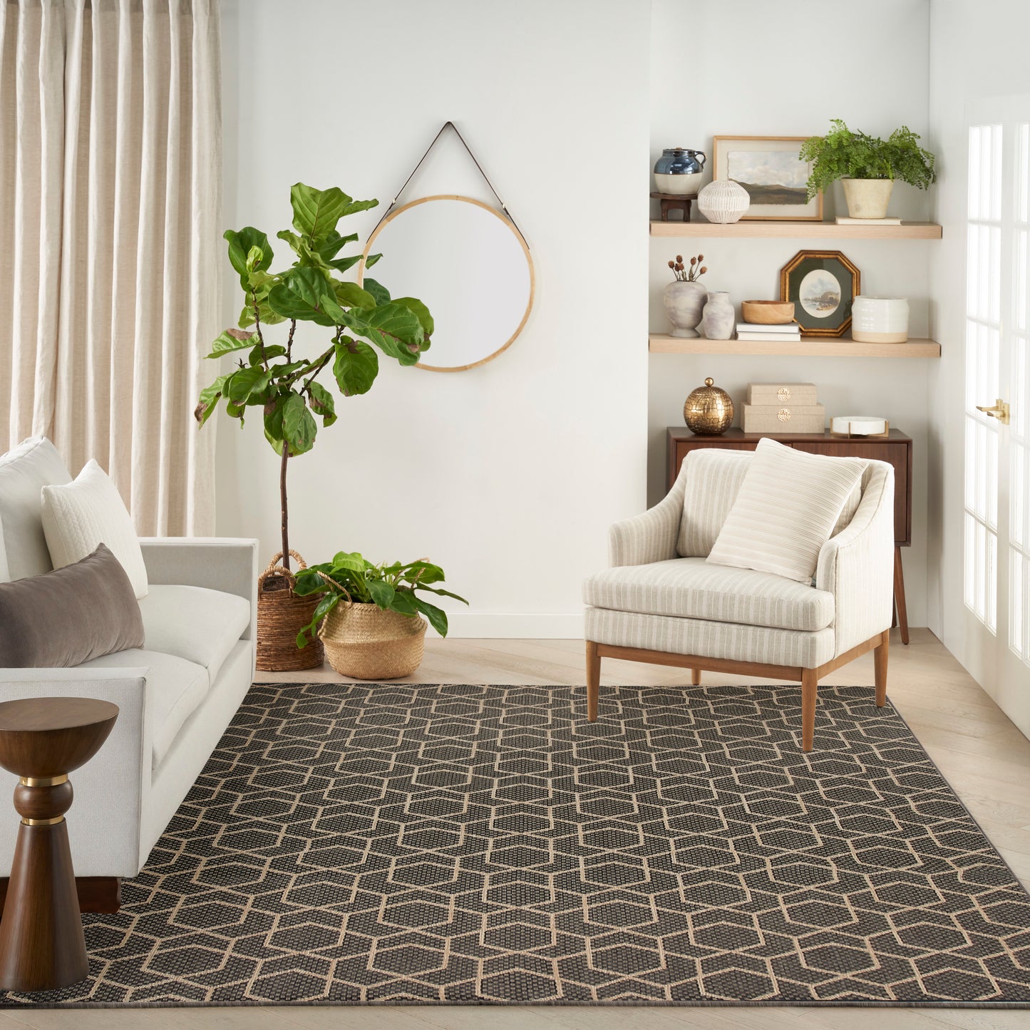 Neutral living room with large leafy plant in woven basket, beige curtains, striped armchair, light sofa, and geometric rug.