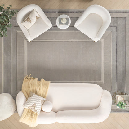 Top-down view of a white living room with a plush sofa, two curved chairs, a small round table, and a gray bordered rug.