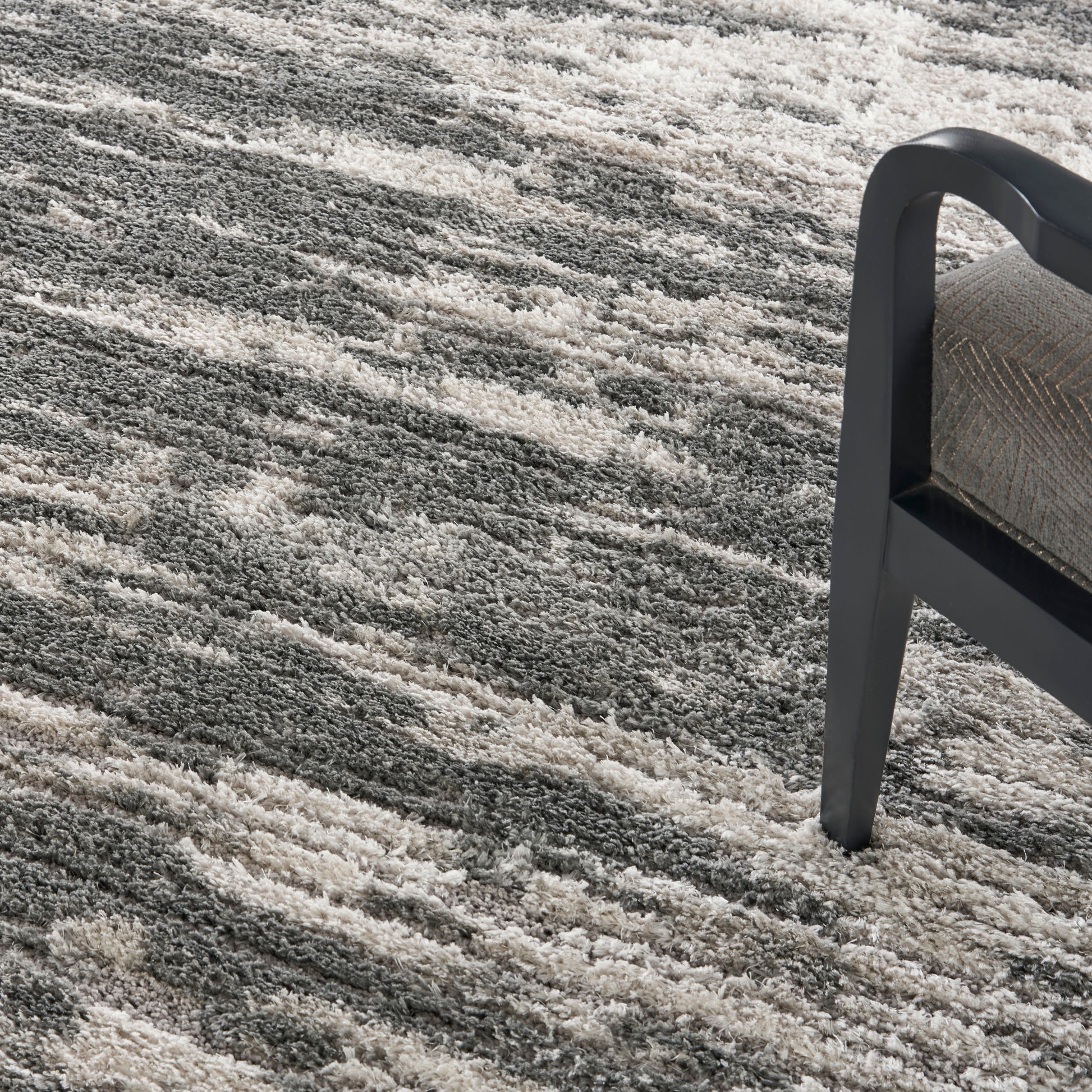 Shaggy gray and beige area rug with a subtle striped pattern, paired with a dark metal-framed chair.