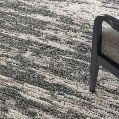 Shaggy gray and beige area rug with a subtle striped pattern, paired with a dark metal-framed chair.
