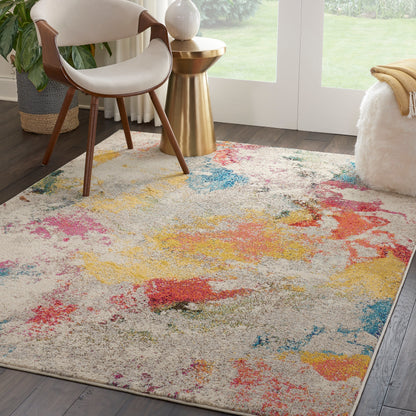 Beige abstract rug with pink, yellow and blue splashes; modern living room with curved cream chair and gold side table.