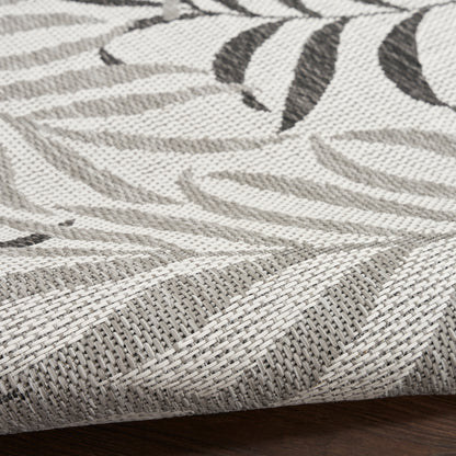 Neutral flat-weave rug with gray leaf pattern on ivory, textured woven fibers, laid on dark wood floor