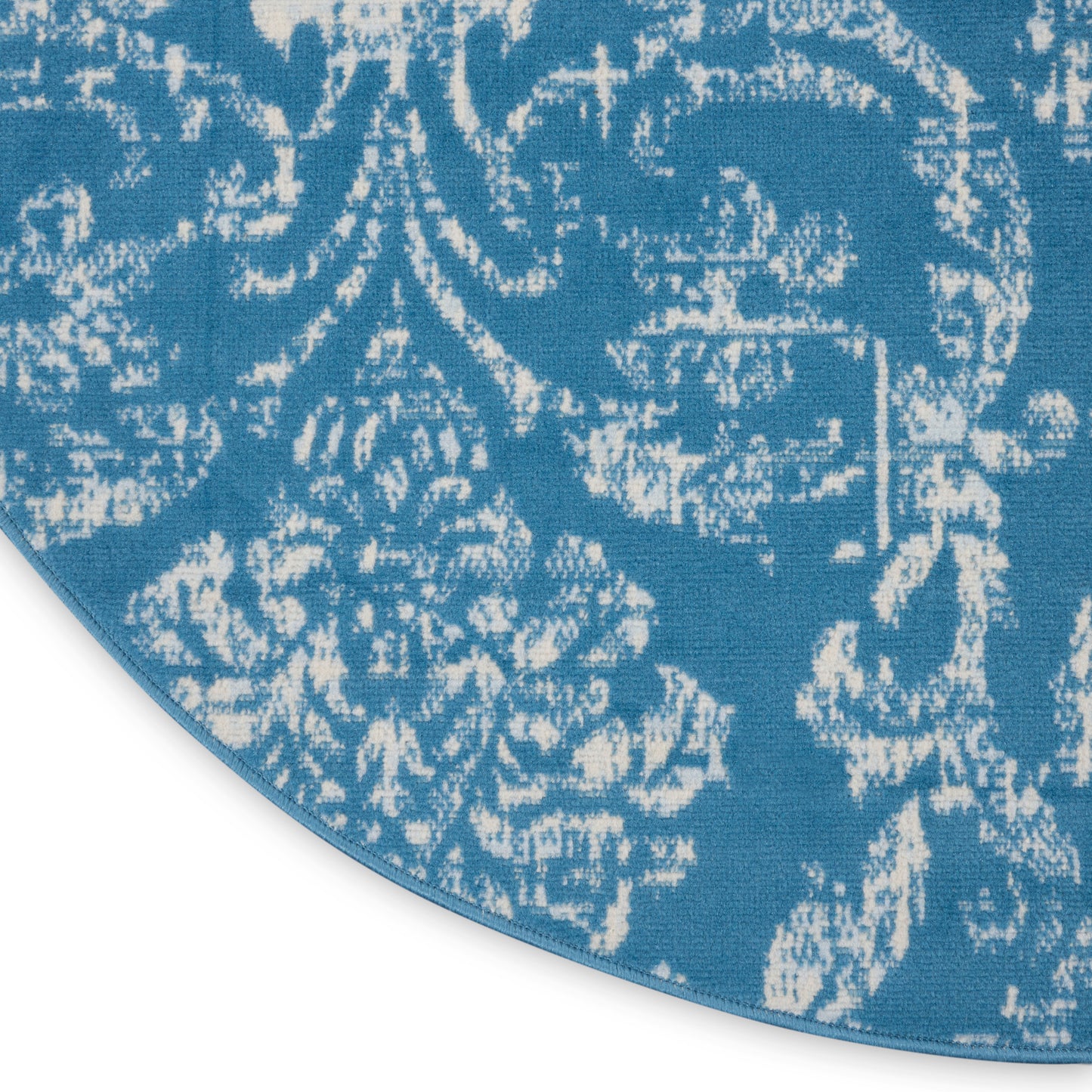Round blue rug with white damask floral pattern; woven textile decorative area rug.