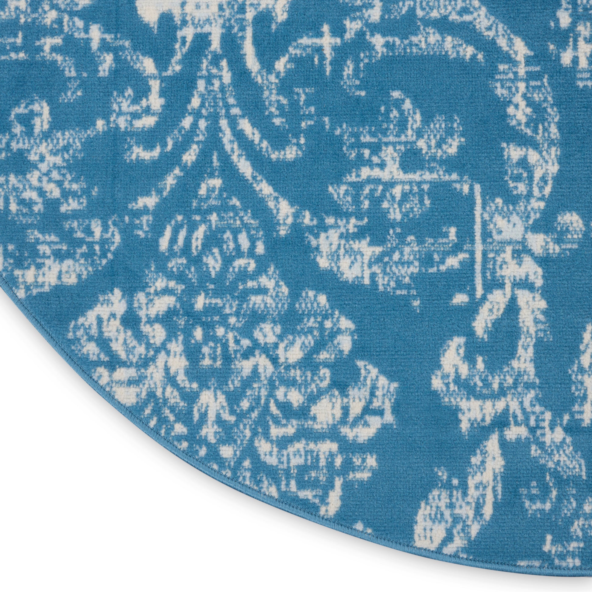 Round blue rug with white damask floral pattern; woven textile decorative area rug.