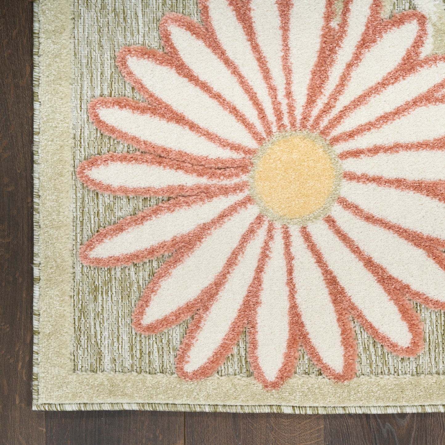 Close-up of a floral rug featuring a large pink-edged daisy, ivory petals, yellow center, and beige border.
