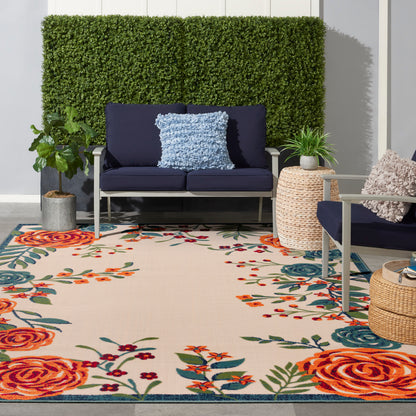 Outdoor rug with a tropical floral pattern on a patio, with a navy-cushioned metal-frame lounge, hedge backdrop, and woven baskets.