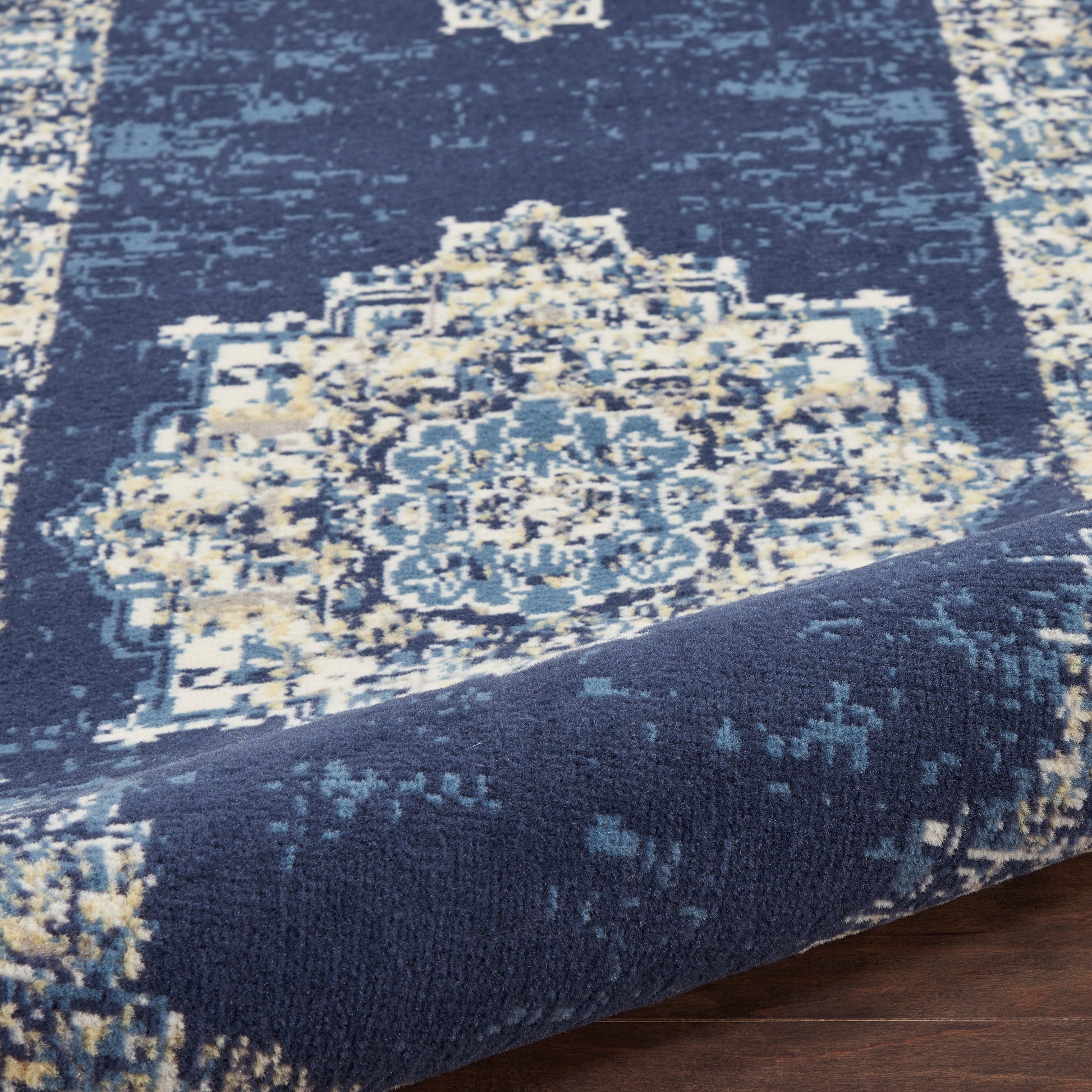 Navy blue oriental area rug with ivory and light-blue medallion pattern, plush woven texture, folded corner.