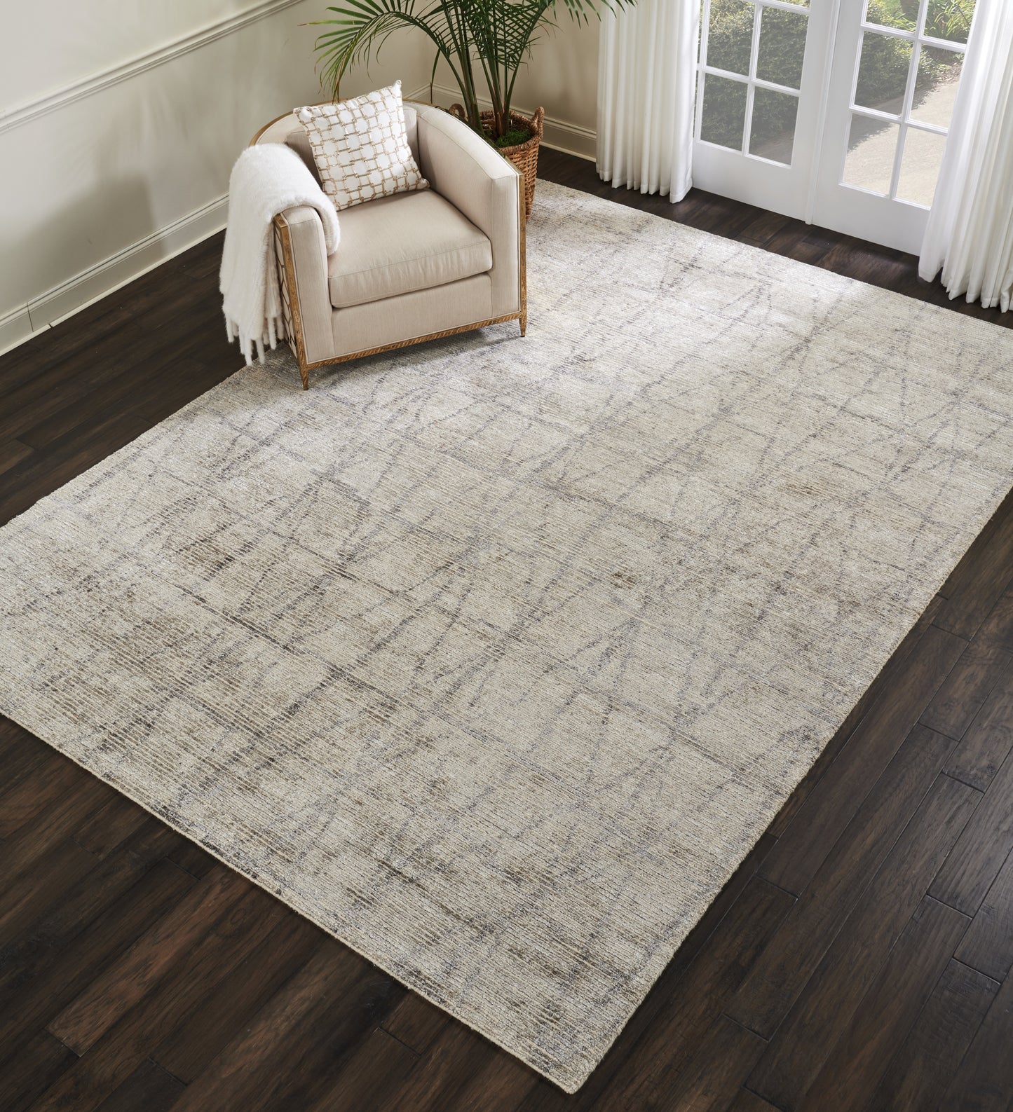 Neutral beige geometric area rug on dark hardwood floor with a beige armchair and plant by a window.
