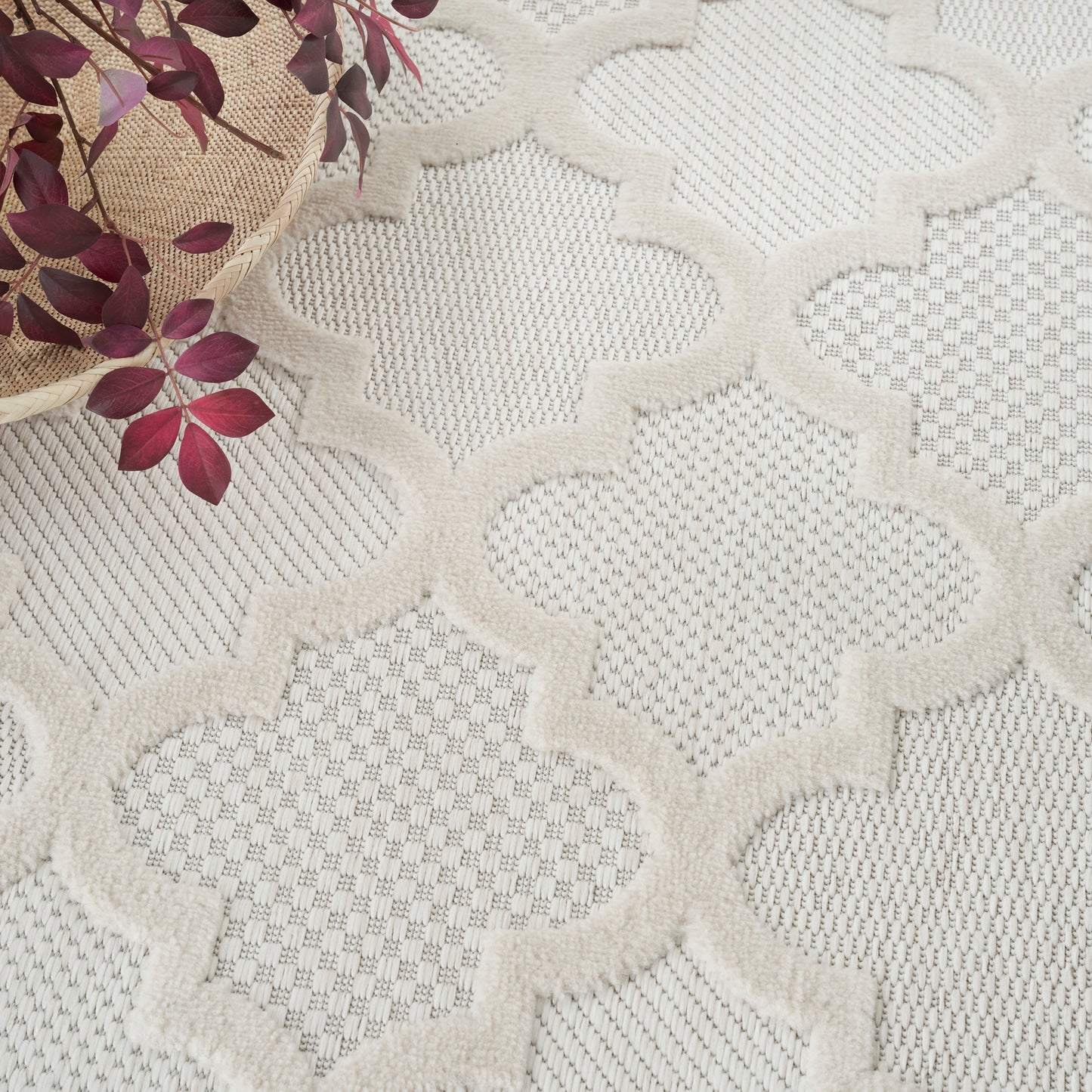 Cream textured rug with raised quattrofoil pattern; woven look beside a straw basket with purple leaves.