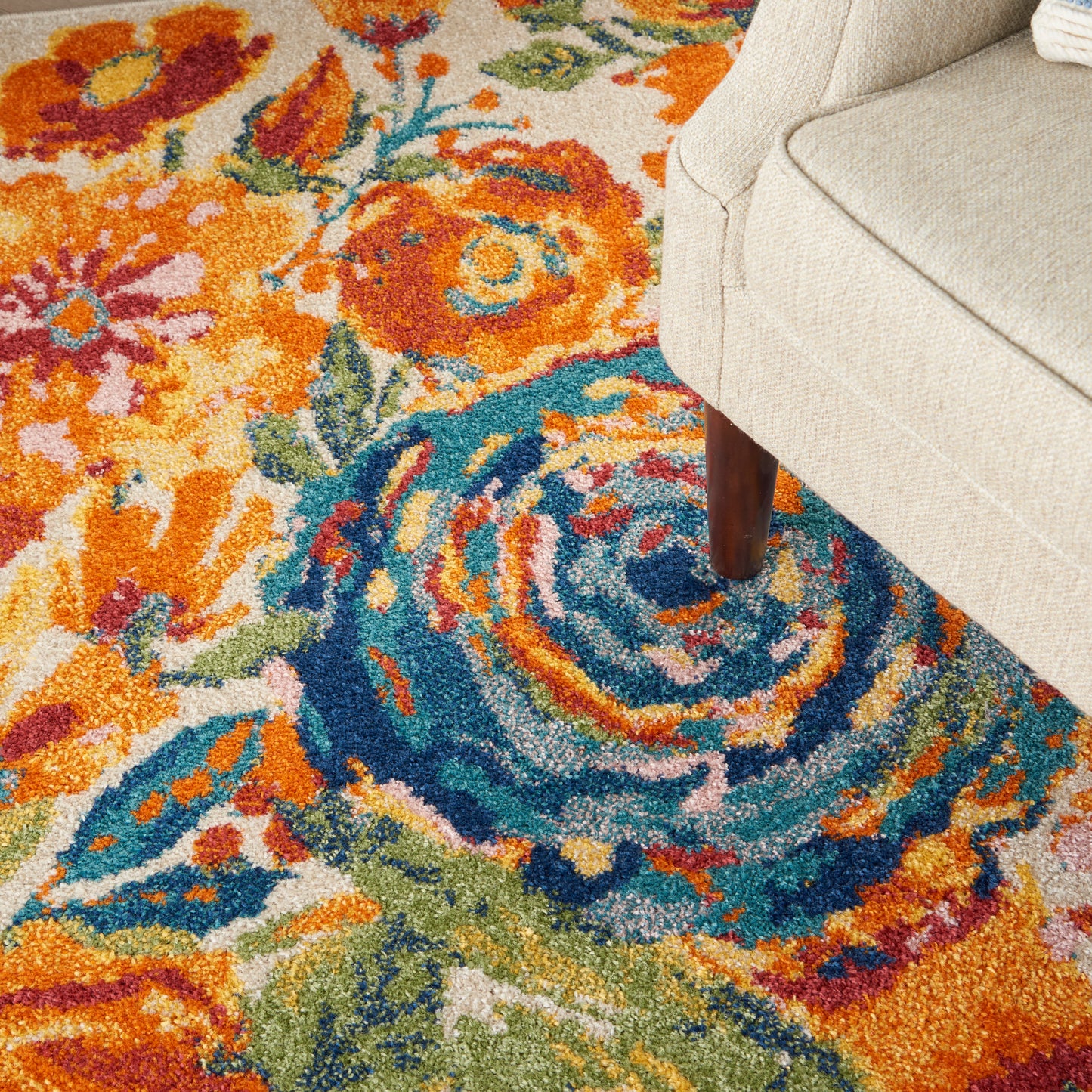 Colorful floral area rug with orange, teal and blue swirls beside a beige upholstered sofa.