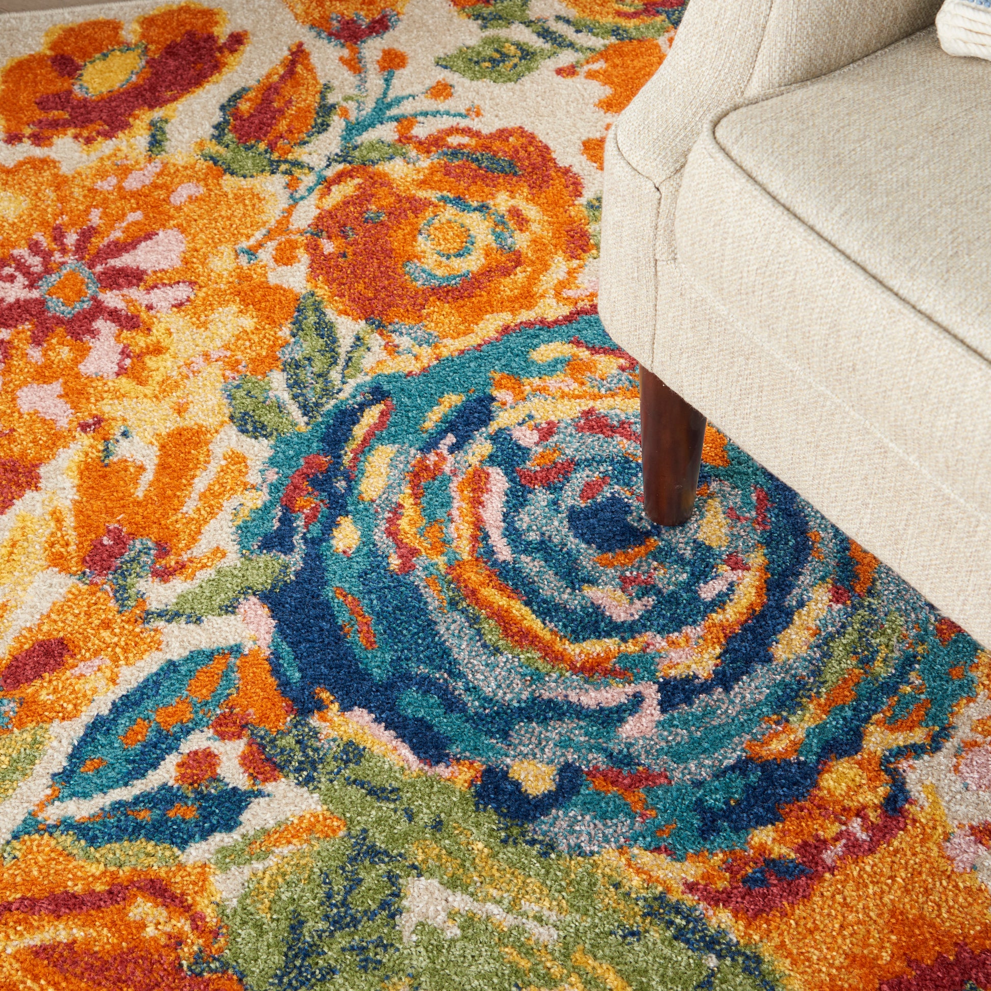Colorful floral area rug with orange, teal and blue swirls beside a beige upholstered sofa.