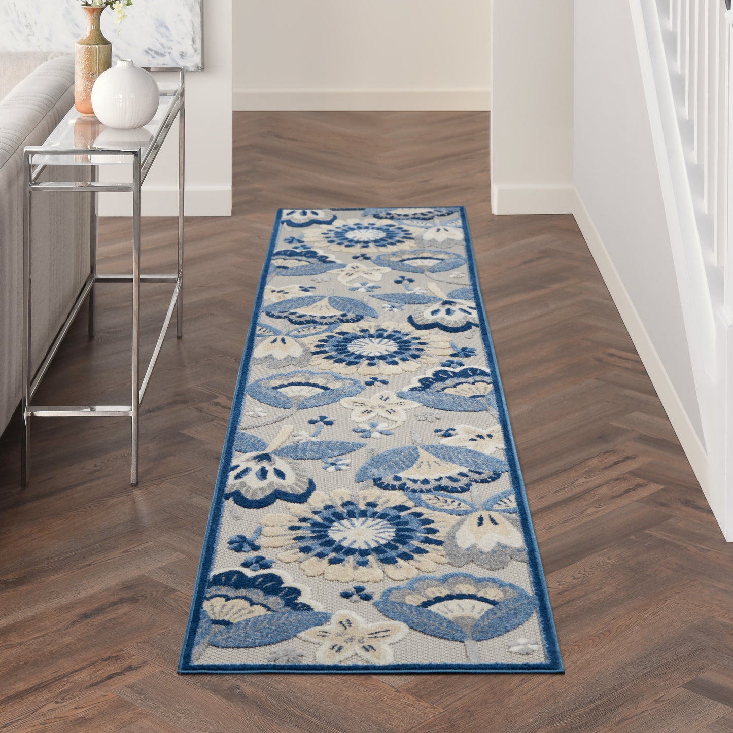 Blue and ivory floral hallway runner rug with a dark blue border on a wood floor beside a glass console table.